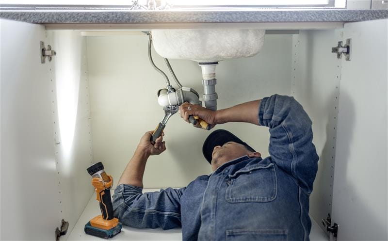 Plumber repairing pipes beneath a bathroom sink in Brandon