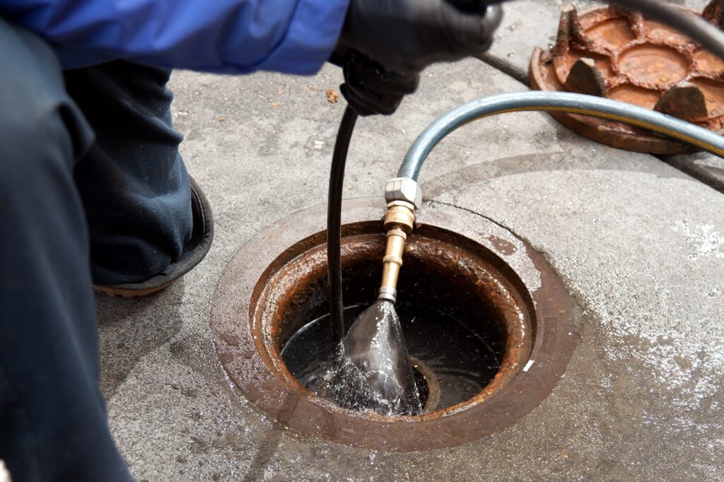 Plumber hydro jetting a sewer line through a manhole in Brandon