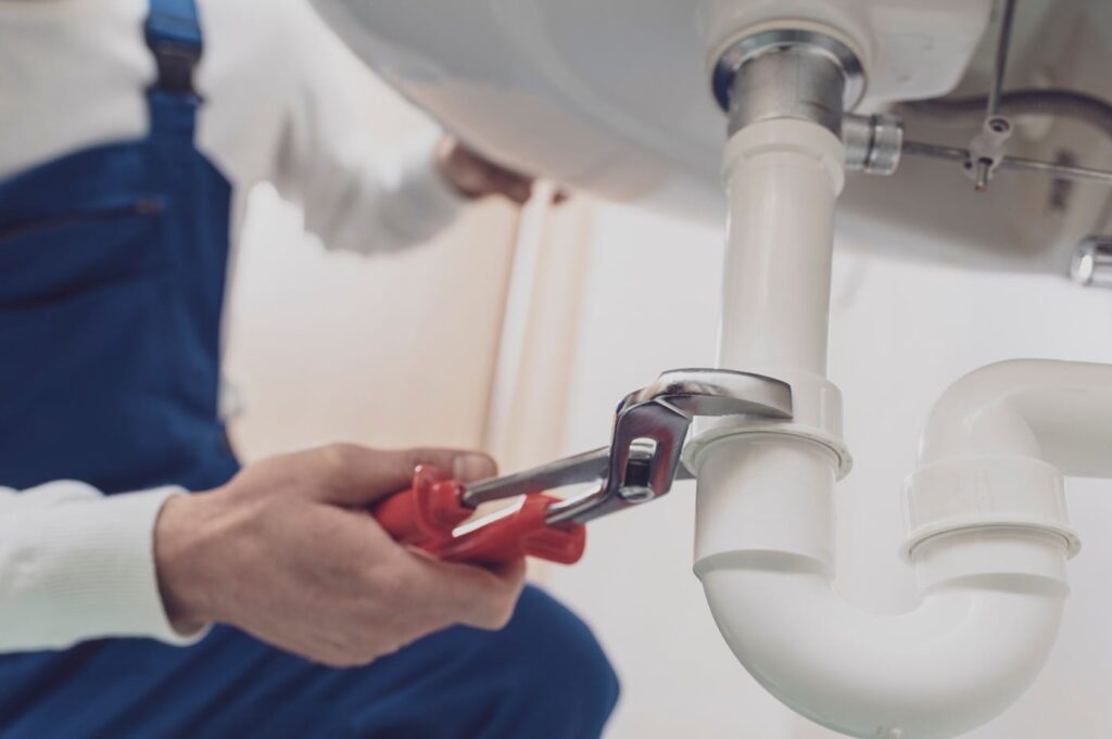 Plumber repairing a white drain pipe beneath a sink in Brandon