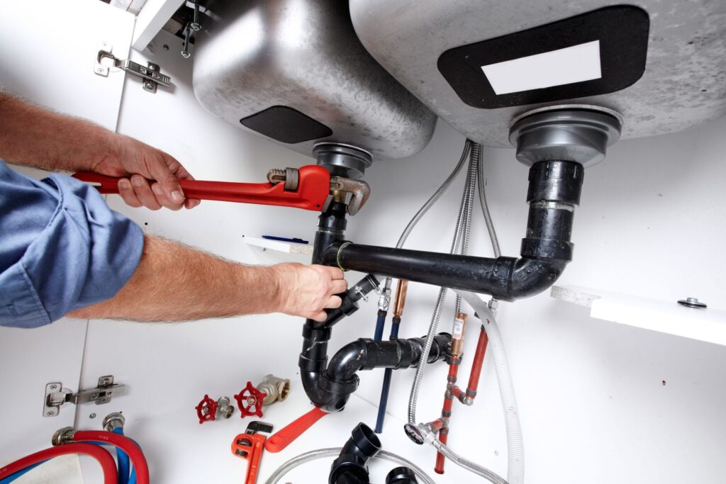 Plumber repairing drain pipes beneath a kitchen sink in Brandon
